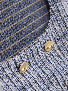 Macro detail of blue tweed fabric texture with decorative gold metal buttons on a vest