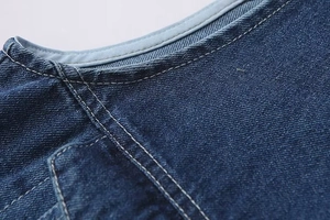 Détail de couture du décolleté en V et texture du tissu denim sergé bleu sur combis