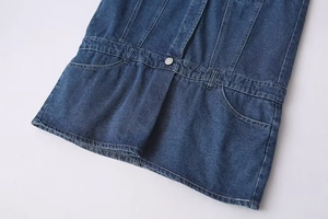 Détail de la taille d'une combinaison en jean bleu foncé avec bouton en métal et poches