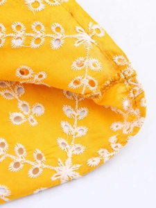 Dettaglio dell'abito giallo con ricamo di margherite bianche e dettagli traforati