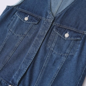 Détail d'un gilet en jean bleu foncé avec poches à rabat et boutons en métal