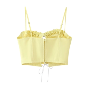 Detailed view of pale yellow crop top with ruffled edges, back zipper, and lace-up ties