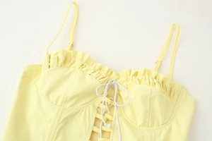 Detail of yellow camisole top with ruffled neckline, adjustable straps, and drawstring tie