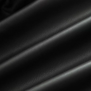 Detailed macro view of black faux leather fabric with soft lychee grain texture and folds