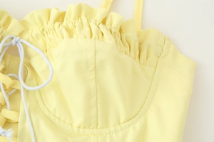 Detail of light yellow top featuring ruffle neckline and white drawstring side tie