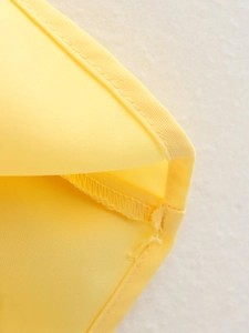 Detailed macro shot of fine stitching and overlock seams on yellow fabric trousers