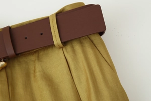 Dettaglio dei pantaloni a vita alta giallo senape con un'ampia cintura in pelle marrone