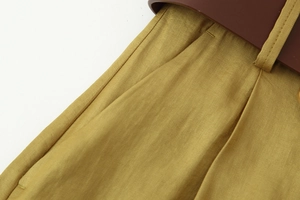 Dettaglio dei pantaloni giallo zenzero con tasche laterali e cintura in pelle marrone
