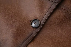 Dettaglio macro di una giacca di pelle marrone con bottone scuro e doppie cuciture rifinite