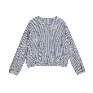 Detail of blue and white striped shirt featuring intricate white floral embroidery on cotton