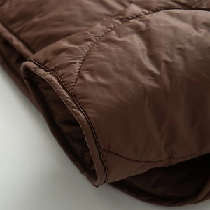 Close-up detail of diamond quilted stitching and hem finish on brown jacket