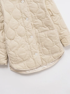 Detail of beige quilted jacket featuring round hem and large square pockets