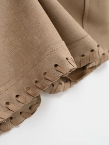 Detail of laser-cut holes and woven straps on brown faux suede vest fabric edge