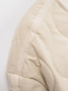 Detail of wavy quilted pattern and woven tape trim on beige winter jacket fabric