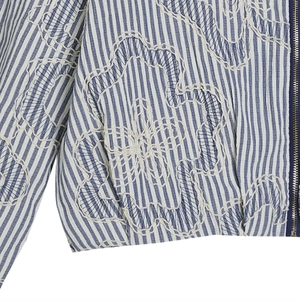Detail of blue striped bomber jacket featuring white floral embroidery and metal zipper