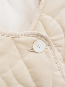 Detail of wavy quilted texture on a beige jacket with a white button and knitted trim