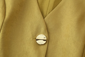 Macro dettaglio del tessuto twill giallo senape e del bottone decorativo in oro martellato