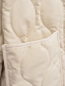 Detail of beige quilted jacket showing wavy stitching and woven trim on the pocket edge