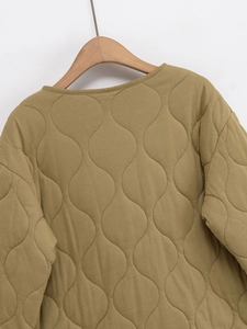 Détail de l'encolure ronde et de la texture matelassée sur une veste jaune moutarde