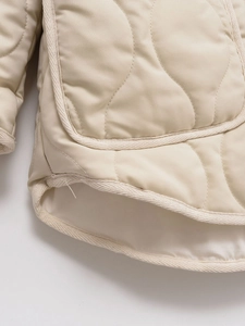 Detail of wavy quilted pattern on beige jacket with rounded hem and high-quality piping
