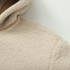 Détail de la texture en peau de mouton beige avec bordure marron sur la veste à capuche