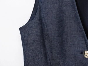 Detail of dark blue linen vest featuring a polished gold button and V-neckline texture
