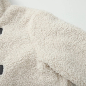Close-up of cream sherpa fleece fabric texture with black leather buckle detail on the coat