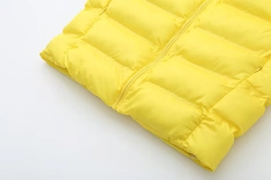 Détail macro du gilet matelassé jaune vif montrant le zip et la texture de la poche