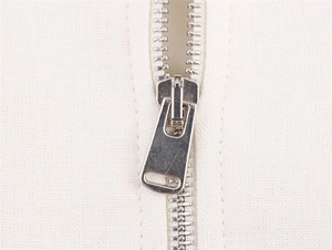 Detailed macro view of silver metal zipper on a khaki jacket with neat stitching detail