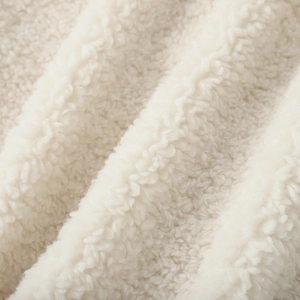 Detailed macro shot of thick faux shearling fabric in warm off-white color and soft texture