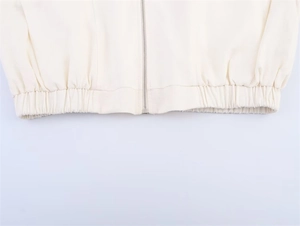 Detailed close-up of the beige jacket elastic hem and silver metallic zipper hardware