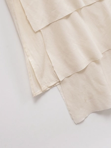 Detail view of tiered cream-colored fabric with natural frayed edges on a summer dress