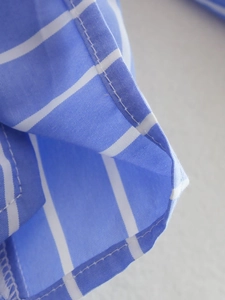 Macro view of blue and white striped fabric with double-folded hem and precise stitching