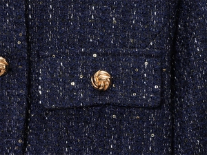 Detail of navy blue tweed jacket fabric with gold sequins and textured metal button