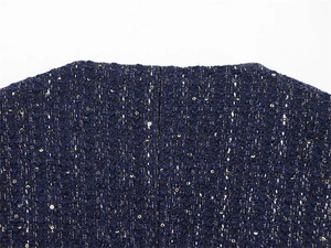 Detail of dark blue tweed fabric with woven texture and gold sequins on the jacket