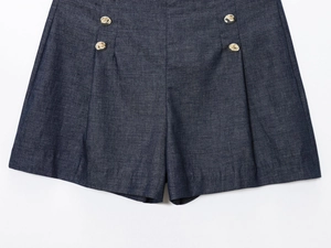Detail of high-waist dark blue denim shorts with decorative gold buttons and pleated hem