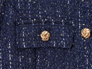 Detailed close-up of navy tweed fabric with golden sequins and spiral metal buttons
