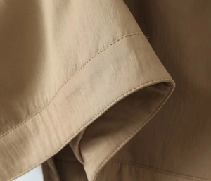 Macro detail of khaki trench coat showing double-stitched cuffs and woven fabric texture