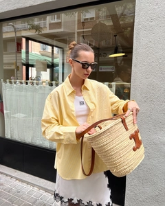 Detail of woven straw tote bag with yellow striped shirt and lace skirt on street