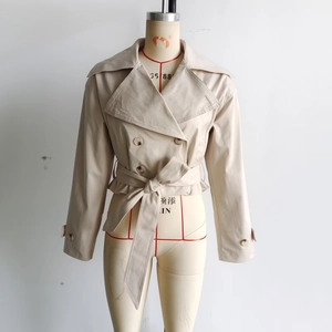 Detail of beige double-breasted trench coat with waist belt bow and buttoned cuffs