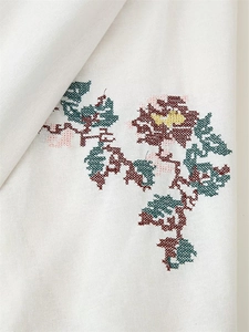 Detailed view of colorful floral cross-stitch embroidery on white cotton fabric