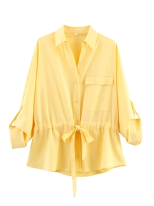 Detail of light yellow long-sleeve shirt featuring a lapel collar and drawstring waist bow