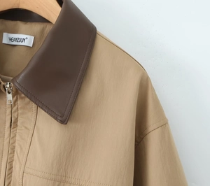 Close-up of khaki trench coat featuring brown leather collar and metal zipper detail