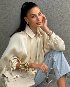 Dettaglio di camicia in seta bianco avorio con jeans blu e borsa in pelle grigia