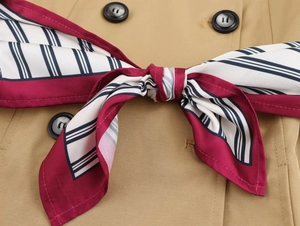 Detail of navy striped silk scarf tied in a bow on a khaki double-breasted trench coat