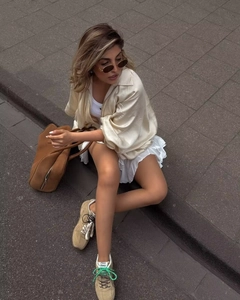 Dettaglio di camicia in seta beige e borsa in pelle marrone pelle con gonna corta a pieghe