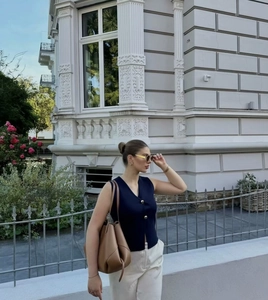 Détail d'un gilet en tricot bleu marine à col en V avec boutons dorés et pantalon blanc