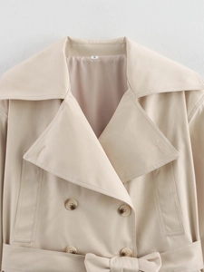Close-up of beige trench coat lapel featuring tortoiseshell buttons and waist tie detail