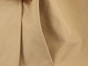 Detailed close-up of khaki trench coat side pocket stitching and high-density twill fabric
