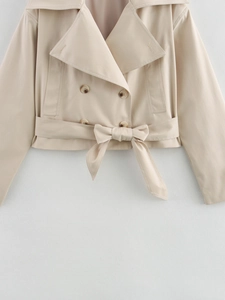Detail of beige double-breasted trench coat featuring lapel collar and waist tie bow